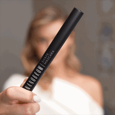 Une femme aux yeux bleus vêtue d'une robe blanche appliquant le mascara Shape